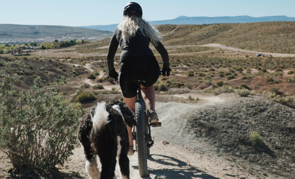 woman riding a bike on a trail with her dog following right behind her
